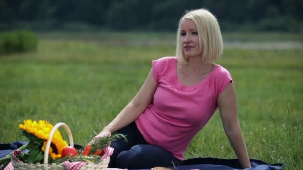 La mujer está sentada y mirando a su alrededor mientras está acostada en una manta de picnic — Vídeo de stock