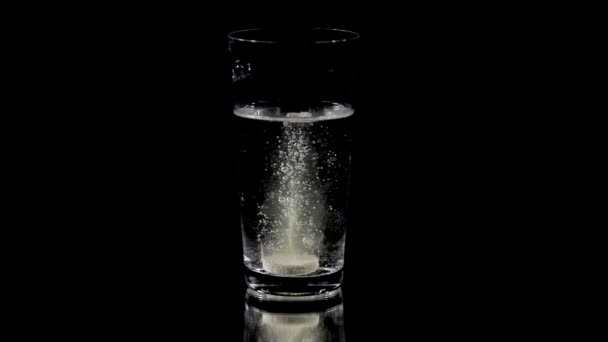 Bubbles from the water-soluble tablet are rising in a glass of water in slow-mo — Stock Video