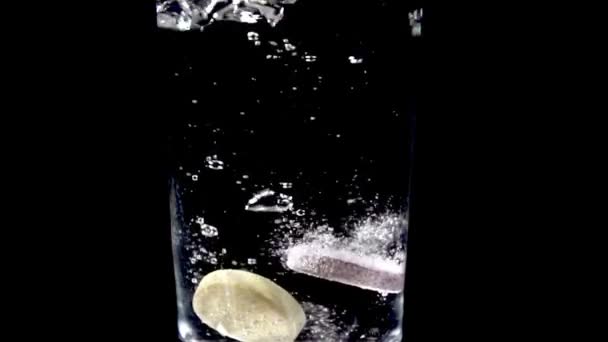 Two vitamin water-soluble tablets start dissolving in a glass of water — Stock Video