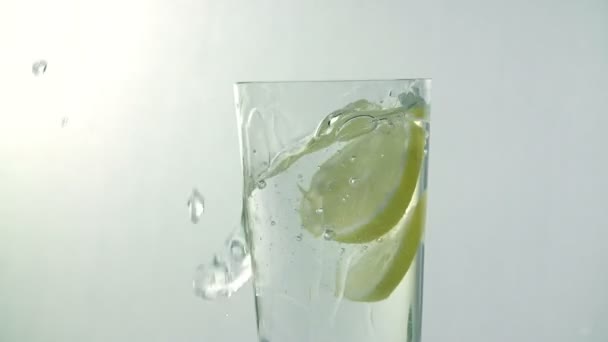 Bitar av citron falla i glas vatten medan vattnet spiller över kanten — Stockvideo