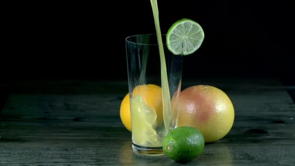 Лимонний сік вливається в склянку з екзотичними фруктами збоку — стокове відео