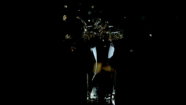 Eiswürfel, die in ein Cola-Glas auf schwarzem Hintergrund fallen