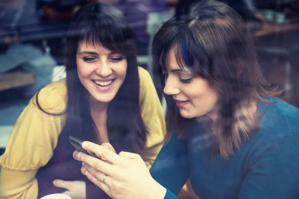 Two girls smiling and using smart phone in a cafe — Stock Photo, Image