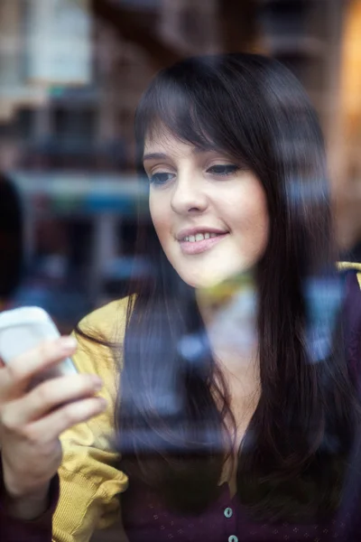 Hermosa chica joven usando el teléfono inteligente en un café — Foto de Stock