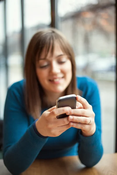 Hermosa chica joven usando el teléfono inteligente en un café — Foto de Stock