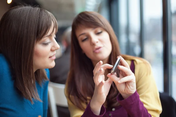 Dos chicas sonriendo y usando un teléfono inteligente en un café — Foto de Stock