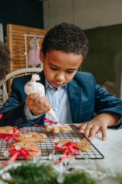 Kız ve erkek kardeş evde masada oturmuş zencefilli ekmek ve kurdele süslüyorlar. Noel zamanı aile eğlencesi konsepti. Bozuk el yapımı Mutlu Yıllar tatlısı, hediye ya da ağaç süslemesi fikri.
