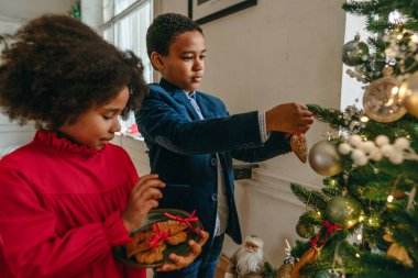 Kız ve erkek kardeş evde kurdeleli zencefilli çörekler asıyorlar. Noel zamanı aile eğlencesi konsepti. El yapımı yeni yıl ağacı süslemesi için bir fikir. Çocuğa odaklan..