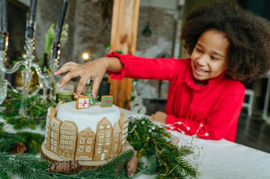 Noel pastasından zencefilli ekmek alan kız ev yapımı zencefilli ekmeklerle süslenmiş. Küçük el yapımı yeni yıl şenlikli şekerlemeler için fikir. Pastanın üzerindeki zencefilli çöreğe odaklan..