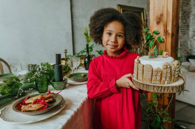 El yapımı zencefilli ev ekmeğiyle süslenmiş Noel pastası tutan kız. On senelik el yapımı Mutlu Yıllar Şenlik Tatlıları.