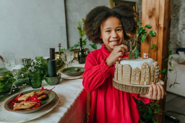 El yapımı zencefilli ev ekmeğiyle süslenmiş Noel pastası tutan kız. On senelik el yapımı Mutlu Yıllar Şenlik Tatlıları.