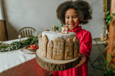 El yapımı zencefilli ev ekmeğiyle süslenmiş Noel pastası tutan kız. Küçük el yapımı yeni yıl şenlikli şekerlemeler için fikir. Pastaya odaklan..