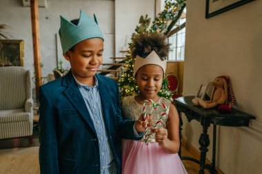 Kız ve erkek kardeş ellerinde Noel şekeri tutuyorlar ve evde kalp şekillendiriyorlar..