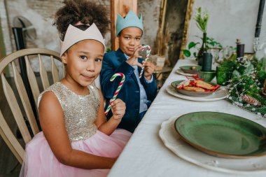 Kız ve erkek kardeş ellerinde Noel şekerleri ile evde masada oturuyorlar..