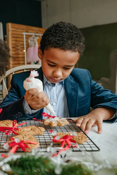 Kız ve erkek kardeş evde masada oturmuş zencefilli ekmek ve kurdele süslüyorlar. Noel zamanı aile eğlencesi konsepti. Bozuk el yapımı Mutlu Yıllar tatlısı, hediye ya da ağaç süslemesi fikri.