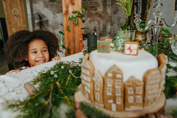 El yapımı zencefilli ev ekmeğiyle süslenmiş Noel pastasına bakan bir kız. Küçük el yapımı yeni yıl şenlikli şekerlemeler için fikir. Kıza odaklan..