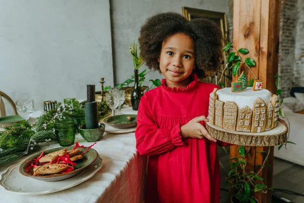 El yapımı zencefilli ev ekmeğiyle süslenmiş Noel pastası tutan kız. On senelik el yapımı Mutlu Yıllar Şenlik Tatlıları.
