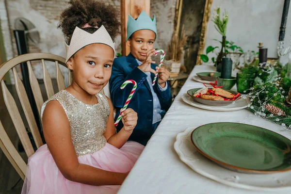 Kız ve erkek kardeş ellerinde Noel şekerleri ile evde masada oturuyorlar..