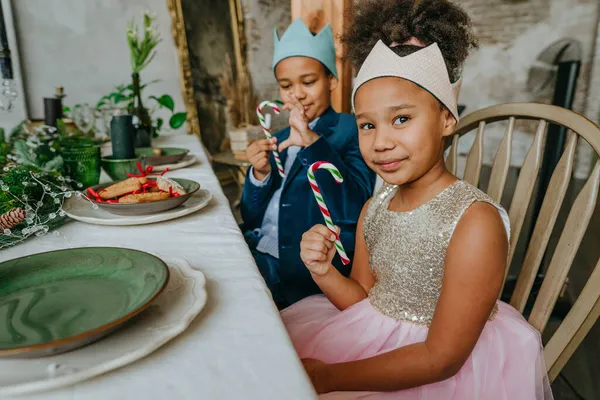 Kız ve erkek kardeş ellerinde Noel şekerleri ile evde masada oturuyorlar..