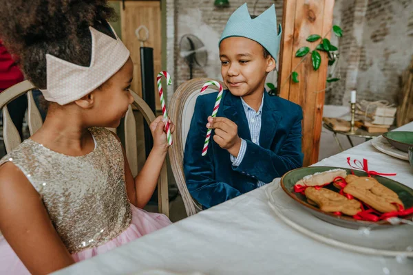 Kız ve erkek kardeş ellerinde Noel şekerleri ile evde masada oturuyorlar..