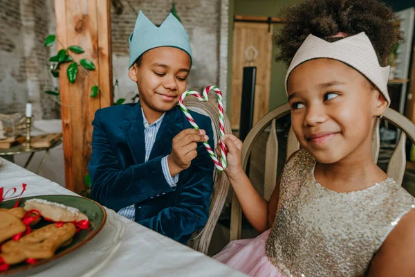 Kız ve erkek kardeş ellerinde Noel şekerleri ile evde masada oturuyorlar..