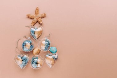 Deniz yıldızı, altın ve mavi boyalı deniz kabuğu ve bej arka planda yosun içeren DIY süslemelerinden yapılmış yaratıcı bir Noel ağacı. Üst manzara, düz uzanma.
