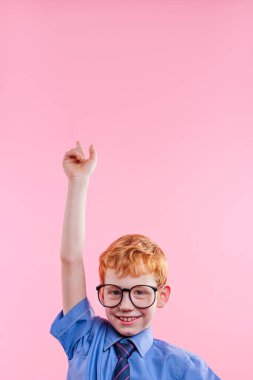 Gözlüklü ve kravatlı küçük bir çocuk pembe arka planda mesaj atmak için boş bir yeri işaret ediyor..