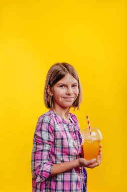 Portakal suyu içen genç bir kız. Sarı arkaplanda metin için boş alan olan stüdyo portresi.