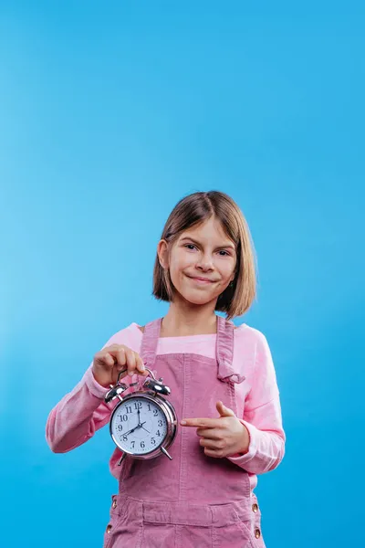 Niña Sosteniendo Reloj Apuntando Sobre Fondo Azul Con Espacio Blanco —  Fotos de Stock