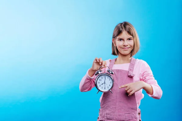 Niña Sosteniendo Reloj Apuntando Sobre Fondo Azul Con Espacio Blanco —  Fotos de Stock