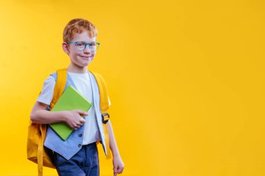 Sırt çantası ve kameraya bakan mutlu ergen çocuk. Sarı arkaplanda metin için boş alan olan stüdyo portresi.