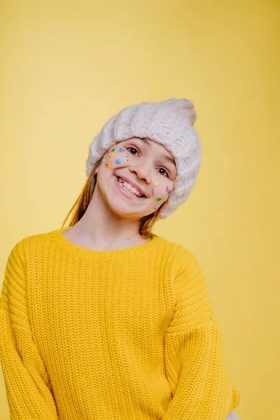 可愛いですティーン女の子とともにステッカーオン彼女の顔身に着けていますピンクニット帽と黄色セーターPosing上の黄色の背景とともに空白のテキスト — ストック写真