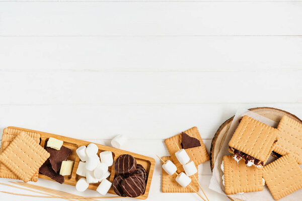 S'mores roasting marshmallows with chocolate between cookies on white wooden background with blank space for text. Top view, flat lay.