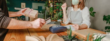 Eko dükkanında kredi kartı kullanarak müşteriyi kapat. POS terminali ve kredi kartı kullanarak yapılan temassız ödeme şekli. Seçici odaklanma. Yatay panoramik pankart.