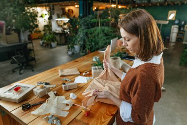 Genç bir kadın atölyesinde kumaş Furoshiki tarzı hediye paketi hazırlıyor. Çevre dostu paket konsepti. Seçici odak.