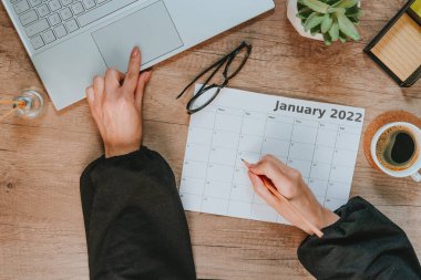 Ocak 2022 'de planlama için takvim kullanan kadınların üst görünümü. Çalışma alanının düzlüğü. Laptoplu ahşap masa, defter. Planlama kavramı.