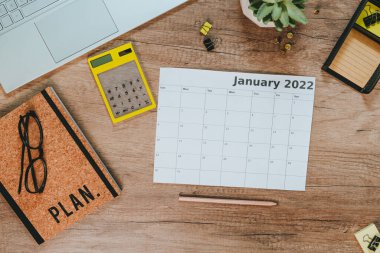 Masraflar ve gelir planlama için Ocak 2022 hesap makinesi ve takviminin en üst görünümü. Çalışma alanının düzlüğü. Laptoplu ahşap masa, defter. Planlama kavramı.