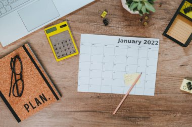 Ocak 2022 tarihli hesap makinesi ve takvim planlama masrafları ve gelirleri için en üst görünüm. Çalışma alanının düzlüğü. Laptoplu ahşap masa, defter. Planlama kavramı.