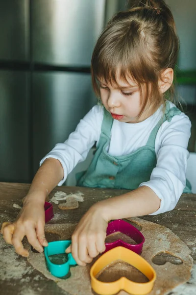 Çavdar hamurundan kalp şeklinde kurabiye kesen küçük kız. — Stok fotoğraf