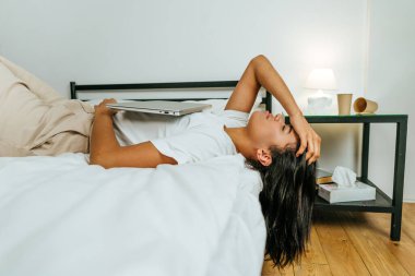 Yatakta dizüstü bilgisayarla yatan genç bir kadın.