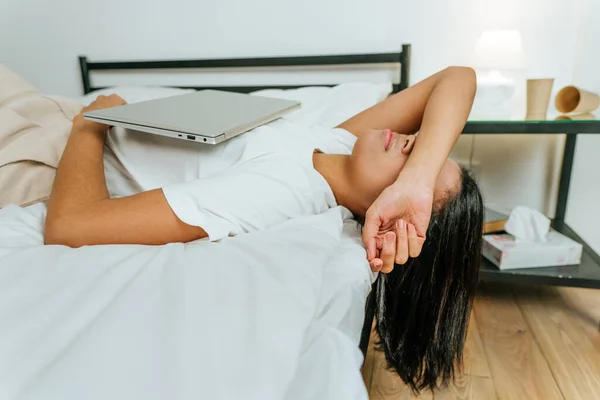 Mujer joven acostada en la cama con un portátil cerrado — Foto de Stock