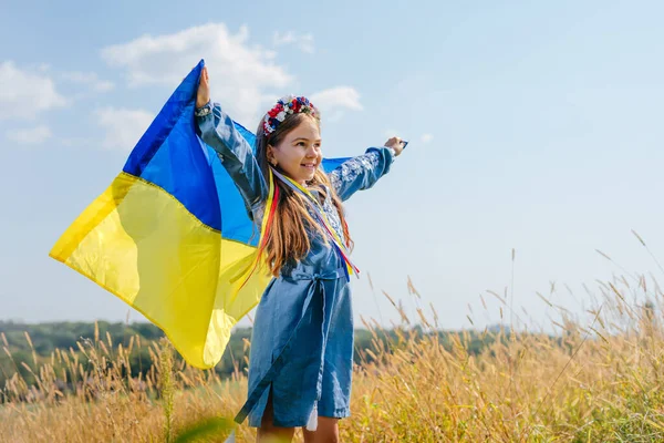 Дівчинка у національній сукні і вінк квітів з прапором України. — стокове фото