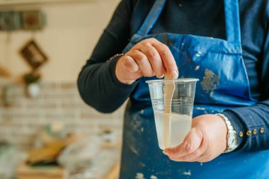 Resin sanat tekniğinde saat yapımında kullanılan malzemeleri hazırlayan sanatçı. Kadın epoksi reçinesinin iki bileşenini karıştırıp kimyasal reaksiyon yaratıyor. Seçici odak.