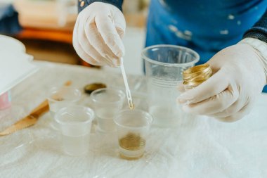 Resin sanat tekniğinde saat yapmak için malzemeleri hazırlayan sanatçı. Plastik eldiven giyen, altın mika tozlu pigmentle orta boyayı karıştıran bir kadın. Seçici odak.