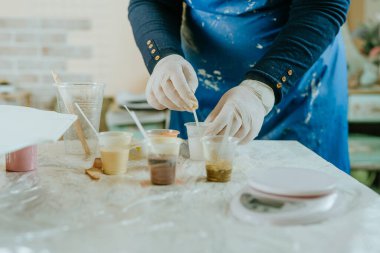 Resin sanat tekniğinde saat yapmak için malzemeleri hazırlayan sanatçı. Lastik eldiven takan kadın reçineye sıvı pigmentler ekliyor. Seçici odak.