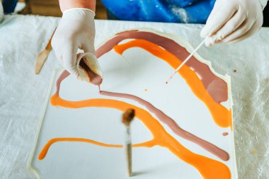 Ressam reçine sanatı tekniğinde saat yapıyor. Lastik eldiven takan kadın pigmentlerle sıvı reçine döküyor. Seçici odak.