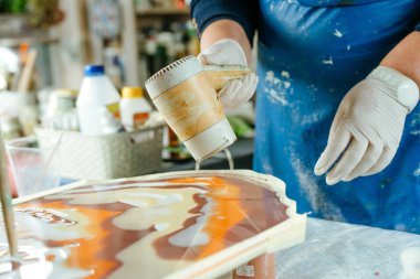 Ressam reçine sanatı tekniğinde saat tahtası yapıyor. Lastik eldiven giyen kadın saç kurutma makinesiyle pigmentli sıvı reçine kullanıyor. Seçici odak.