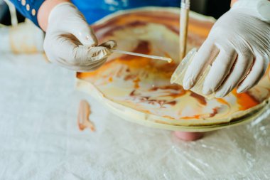 Ressam reçine sanatı tekniğinde saat yapıyor. Lastik eldiven takan kadın pigmentlerle sıvı reçine döküyor. Seçici odak.