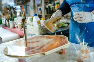 Ressam reçine sanatı tekniğinde saat tahtası yapıyor. Lastik eldiven giyen kadın saç kurutma makinesiyle pigmentli sıvı reçine kullanıyor. Seçici odak.