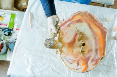 Ressam reçine sanatı tekniğinde saat tahtası yapıyor. Lastik eldiven giyen kadın saç kurutma makinesiyle pigmentli sıvı reçine kullanıyor. Seçici odak.